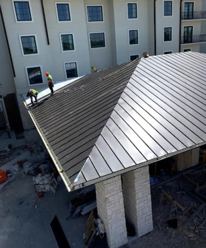 Crew installing standing seam metal roof panels on a commercial project in DeKalb
